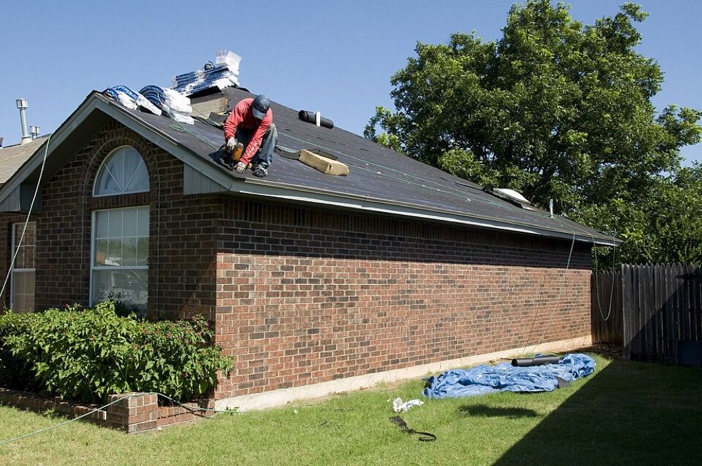 A roofer installing new shingles on a storm-damaged residential roof
